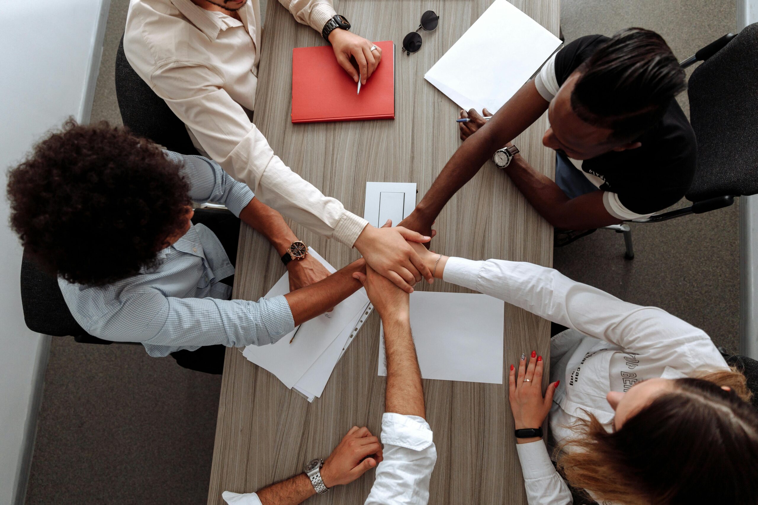 Overhead view of a diverse team placing hands together in a sign of unity during a meeting.